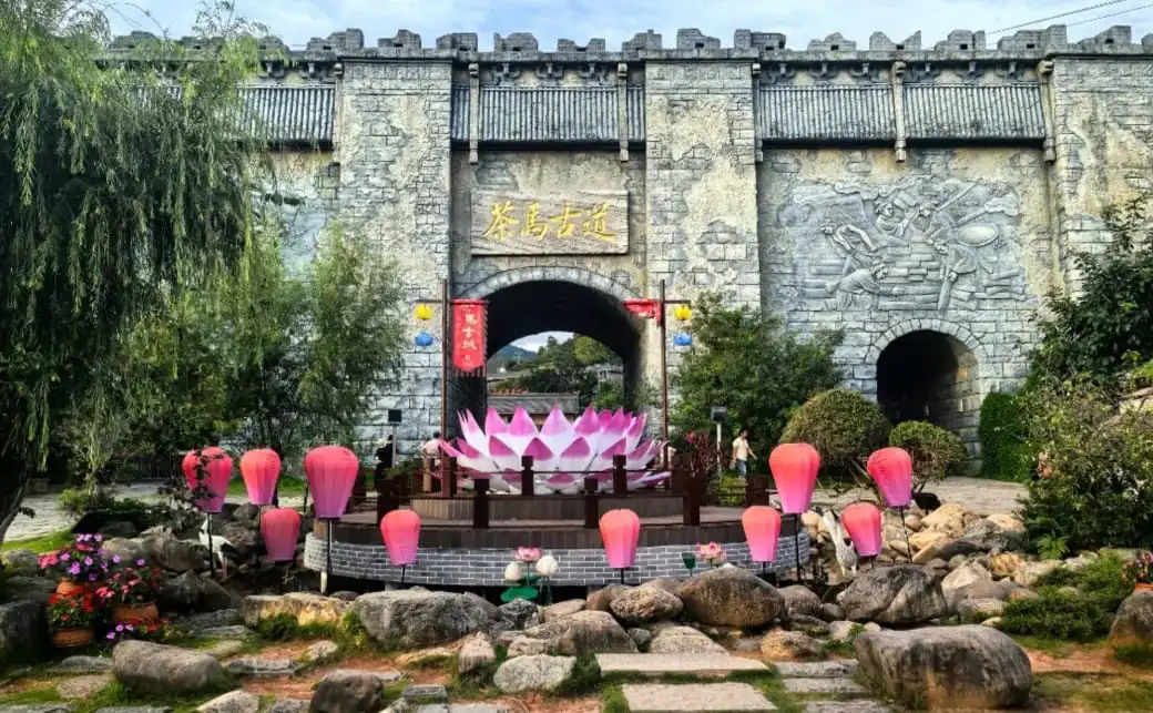 Puge Tea Horse Road Adventure,Shangri-La,Chinatour Stone fortress gate with arched entrance, Chinese-sign plaque, surrounded by pink lotus lanterns and a large pink lotus sculpture.