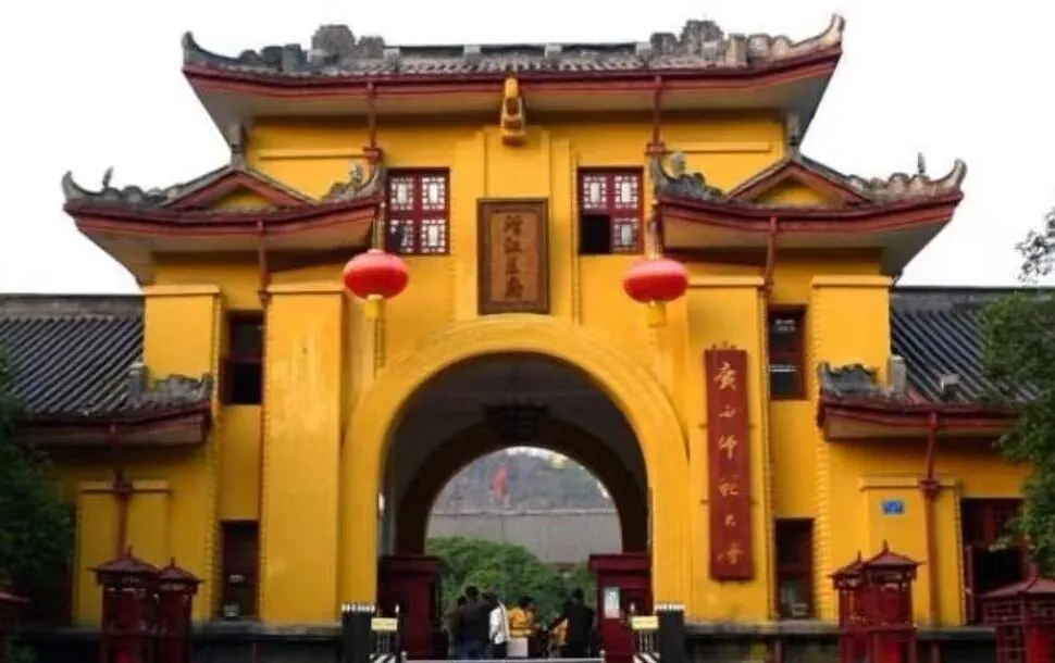 Yellow Chinese-style gate with curved roofs, red lanterns, and a central arch leading to a courtyard; people enter the site.Jingjiang Princes’ City,Guilin,Guangxi ,Chinatravel
