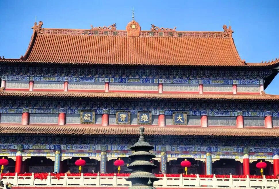 Front view of a traditional Chinese temple with blue and gold detailing, red columns, and a tiered roof under a clear blue sky, with red lanterns along the walkway.Kaifu Temple,Changsha,Hunan ,Chinatravel