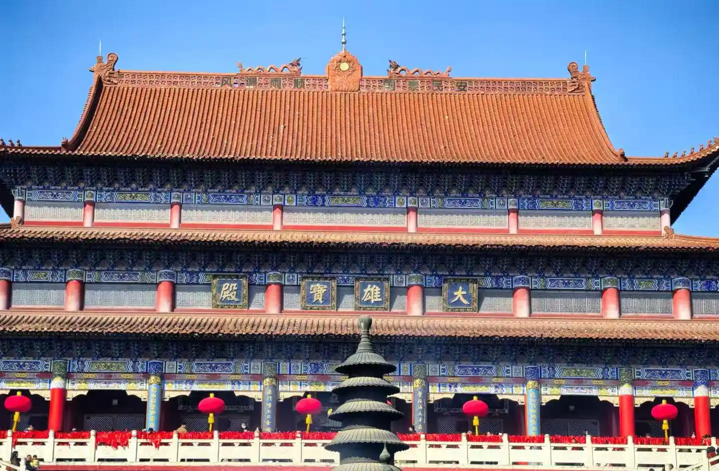 Front view of a traditional Chinese temple with blue and gold detailing, red columns, and a tiered roof under a clear blue sky, with red lanterns along the walkway.Kaifu Temple,Changsha,Hunan ,Chinatravel