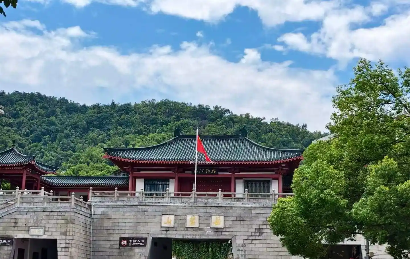 Traditional Chinese temple complex on a stone gate with red walls and a dark tiled roof, flagpole with a red flag against green hills and blue sky.Yuelu Mountain Park,Changsha,Hunan ,Chinatravel