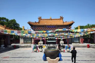 Traditional Chinese temple courtyard with a pagoda-style roof, colorful prayer flags, and a large bronze incense burner in the foreground.Dazhao Temple,Hohhot,Inner Mongolia