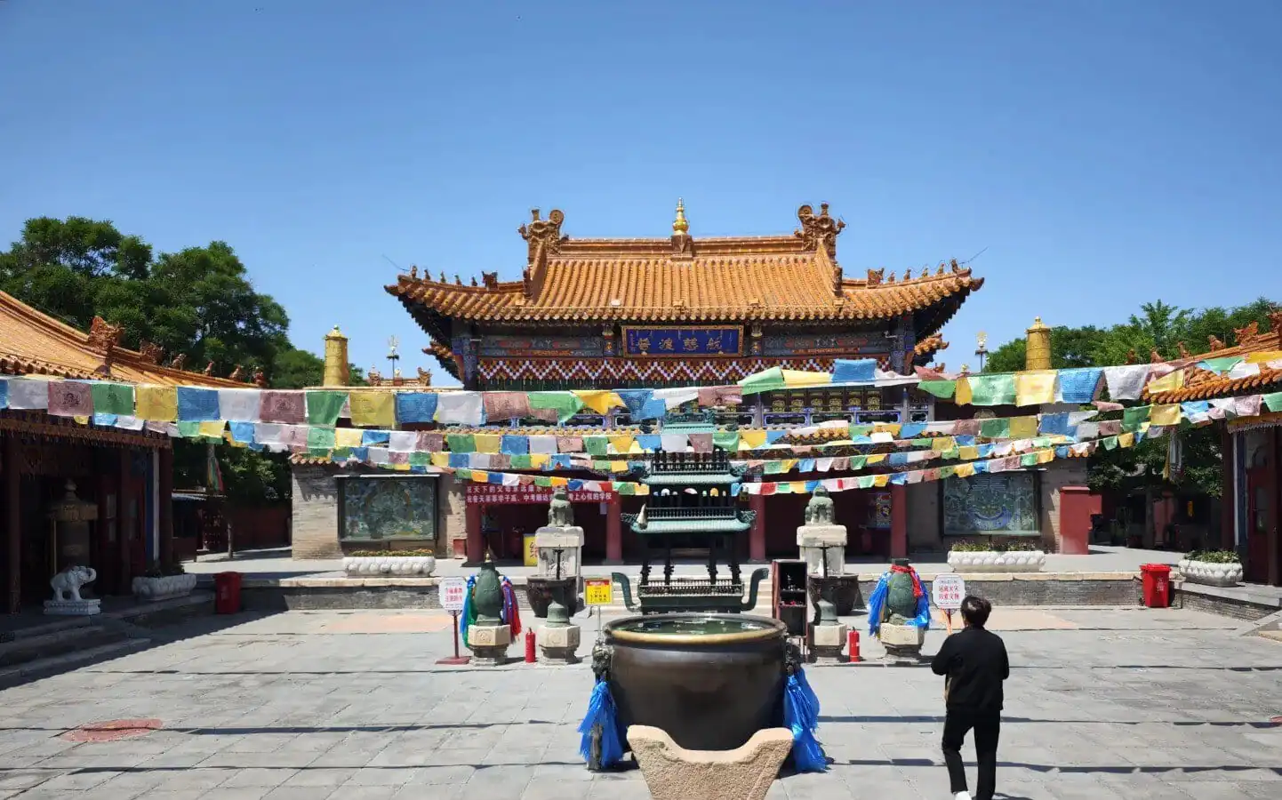 Traditional Chinese temple courtyard with a pagoda-style roof, colorful prayer flags, and a large bronze incense burner in the foreground.Dazhao Temple,Hohhot,Inner Mongolia
