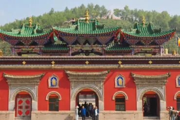 Red temple facade with ornate arched doorways and colorful, tiered roofs; visitors enter through central arch.Ta’er Monastery Kumbum Monastery,Xining,Qinghai