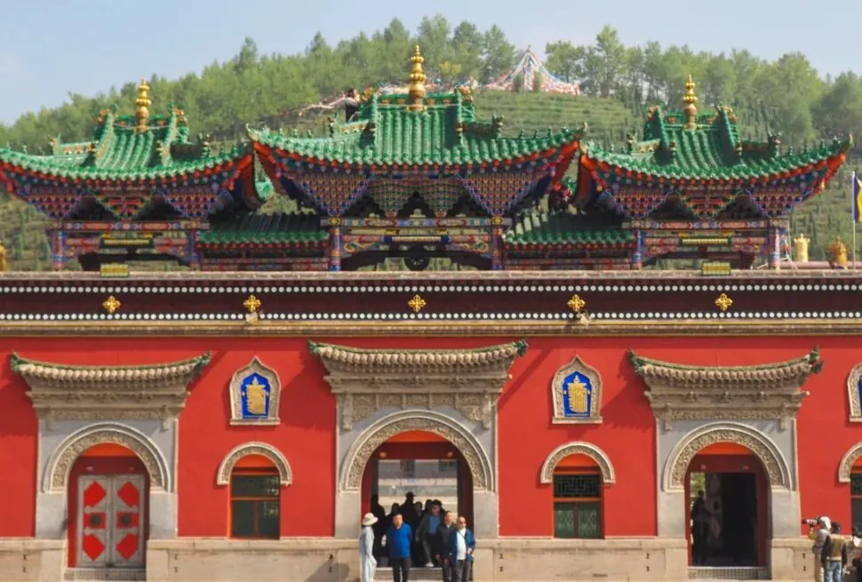 Red temple facade with ornate arched doorways and colorful, tiered roofs; visitors enter through central arch.Ta’er Monastery Kumbum Monastery,Xining,Qinghai