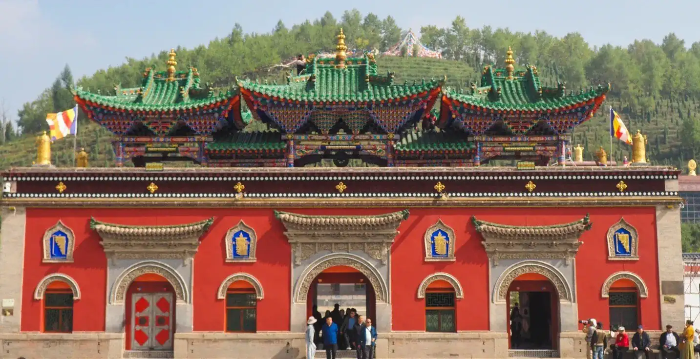 Red temple facade with ornate arched doorways and colorful, tiered roofs; visitors enter through central arch.Ta’er Monastery Kumbum Monastery,Xining,Qinghai