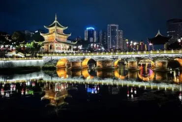 Night scene of a lit traditional Chinese pagoda and arched bridge over a calm river with reflections in the water.Jiaxiu Tower,Guiyang,Guizhou