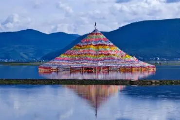 Colorful pyramid of prayer flags floating on a calm lake with mountain hills in the background, reflecting in the water,Napahai Lake,Shangri-La,Yunnan,Chinatravel