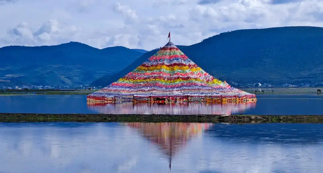 Colorful pyramid of prayer flags floating on a calm lake with mountain hills in the background, reflecting in the water,Napahai Lake,Shangri-La,Yunnan,Chinatravel