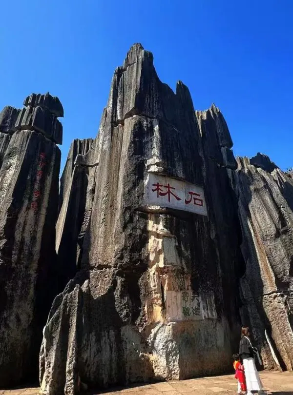 Tall jagged rock formations rise against a bright blue sky, with a white sign bearing red Chinese characters in the center. (informative)Kunming Stone Forest,Kunming,Yunnan ,Chinatravel