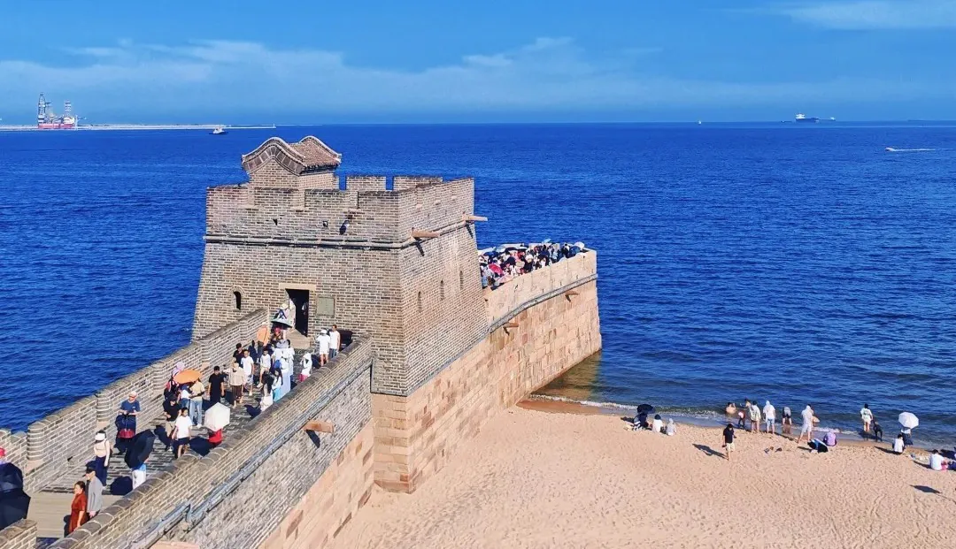 Stone coastal fortress with a walkway filled with visitors along the wall, overlooking a calm blue sea on a sunny day.Shanhaiguan,Qinhuangdao,Hebei,Chinatravel