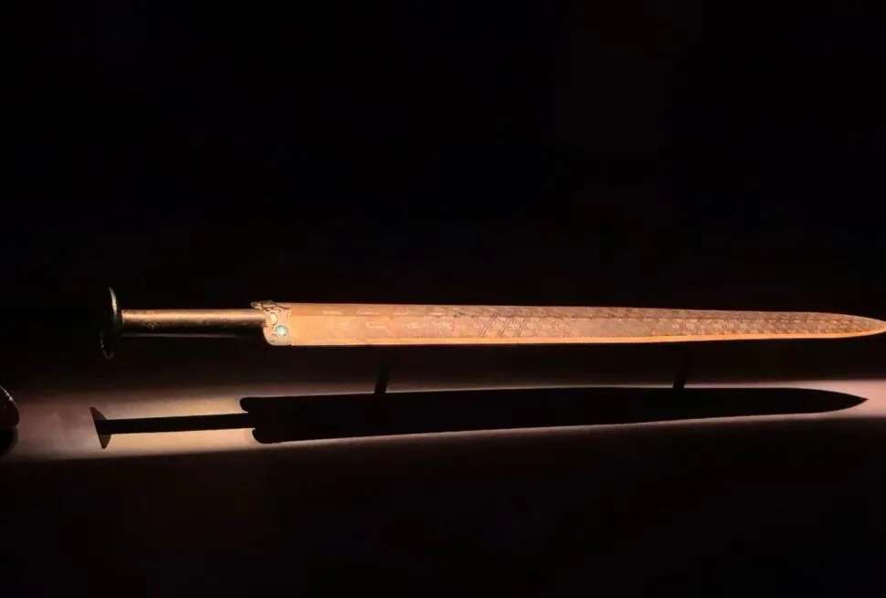 Ornate dagger with a metal hilt and long slim blade, placed above a brown sheath on a dark surface.Hubei Provincial Museum,Wuhan,Hubei ,Chinatravel