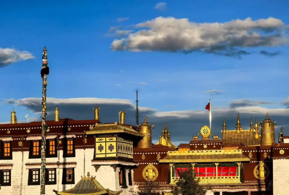 Golden Tibetan temple complex with gilded rooftops, prayer wheels, and decorated poles against a bright blue sky with scattered clouds,Jokhang Temple,Lhasa,Tibet,Chinatravel