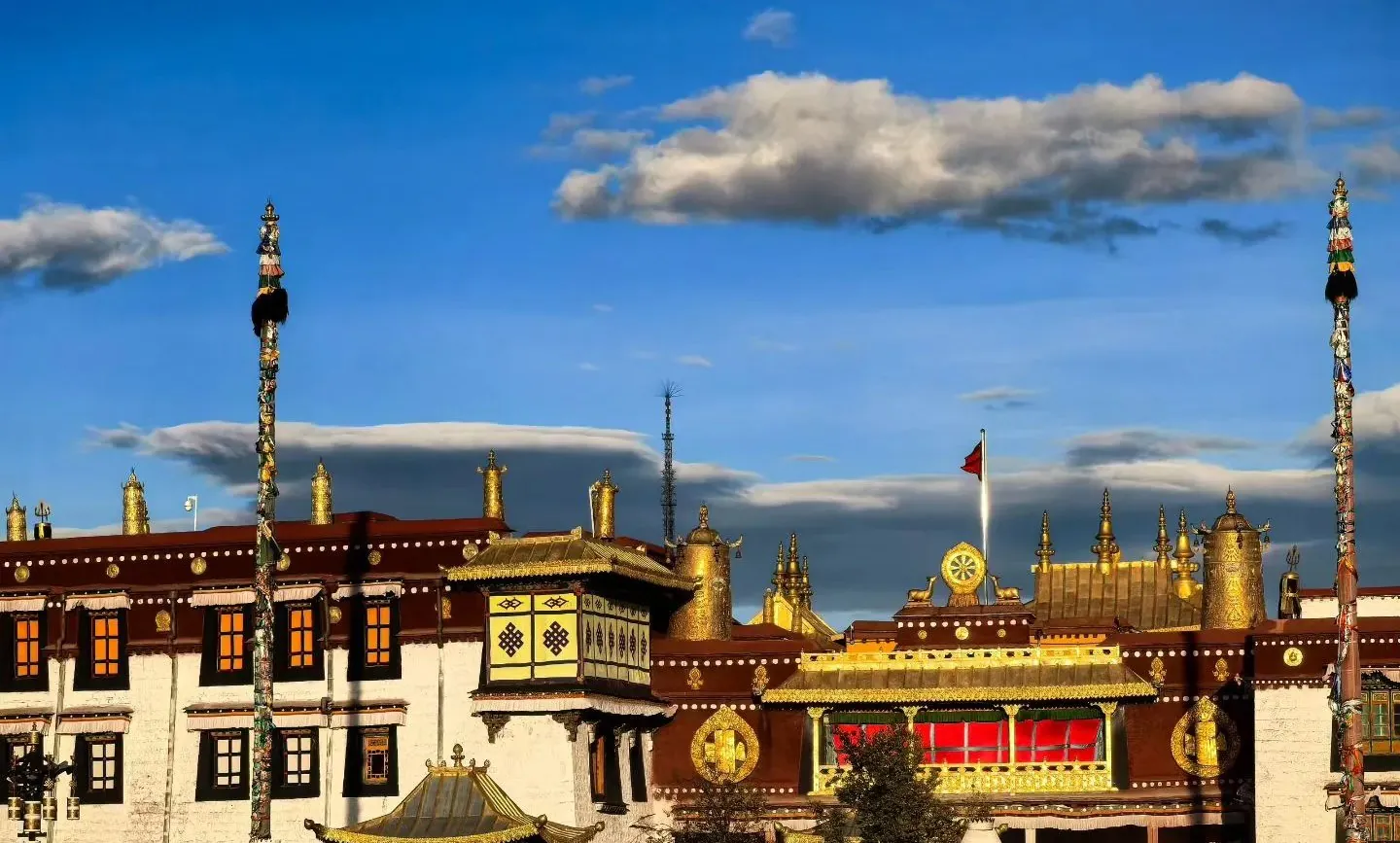 Golden Tibetan temple complex with gilded rooftops, prayer wheels, and decorated poles against a bright blue sky with scattered clouds,Jokhang Temple,Lhasa,Tibet,Chinatravel
