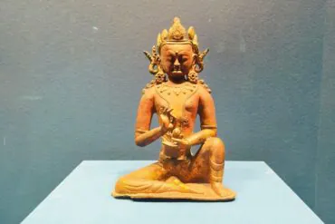 Terracotta statue of a seated deity on a blue pedestal, hands in a mudra gesture, against a blue wall.Hohhot Inner Mongolia Museum,Hohhot,Inner Mongolia,Chinatravel