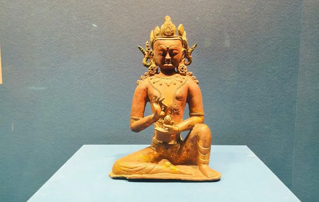 Terracotta statue of a seated deity on a blue pedestal, hands in a mudra gesture, against a blue wall.Hohhot Inner Mongolia Museum,Hohhot,Inner Mongolia,Chinatravel