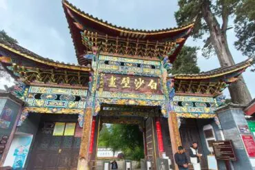 Colorful traditional Chinese temple gate with gold lettering, intricate carvings, and a doorway flanked by visitors.Baisha Village,Lijiang,Yunnan,Chinatravel