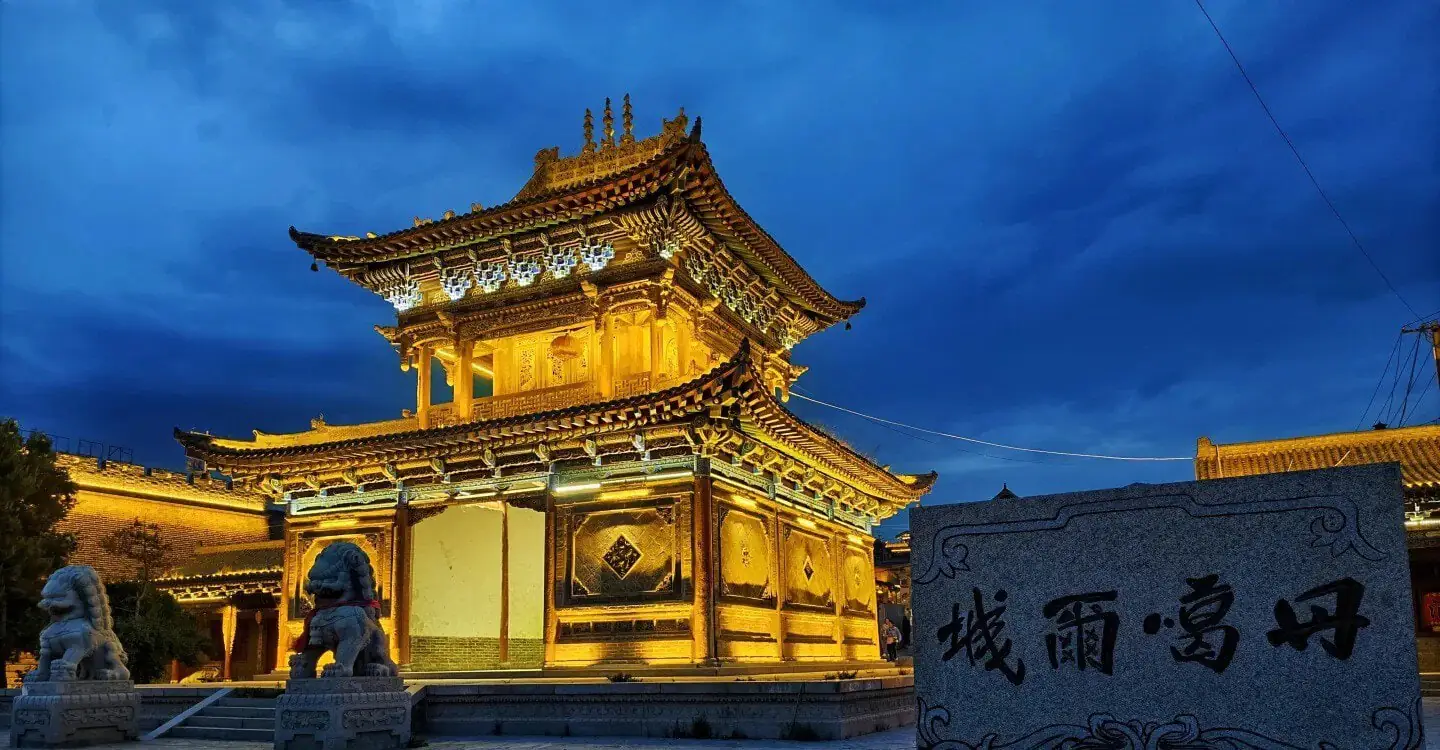 Illuminated ancient Chinese temple gate with ornate, multi-tiered roof at dusk, flanked by stone lion statues.Donggar Ancient City,Xining,Qinghai