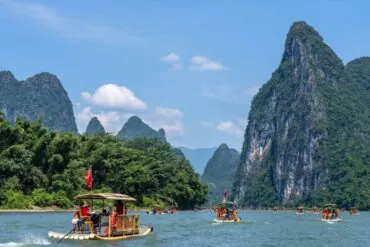 Bamboo boats with passengers on a wide river, surrounded by towering green karst mountains under a bright blue sky.Li River,Guilin,Guangxi ,Chinatravel