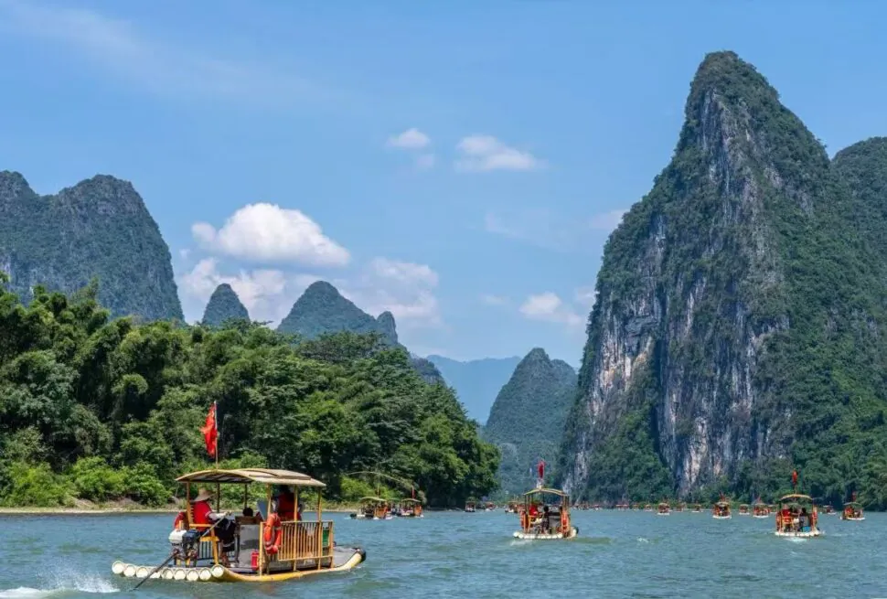 Bamboo boats with passengers on a wide river, surrounded by towering green karst mountains under a bright blue sky.Li River,Guilin,Guangxi ,Chinatravel