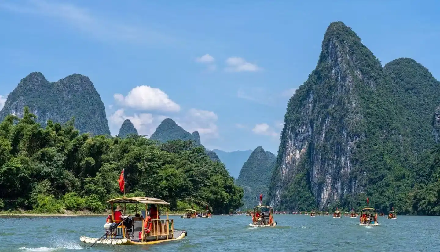 Bamboo boats with passengers on a wide river, surrounded by towering green karst mountains under a bright blue sky.Li River,Guilin,Guangxi ,Chinatravel