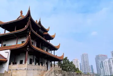 Traditional multi-story Chinese temple with ornate orange-tiled roofs in the foreground and modern high-rise buildings in the background under a blue sky.Tianxin Pavilion,Changsha,Hunan ,Chinatravel