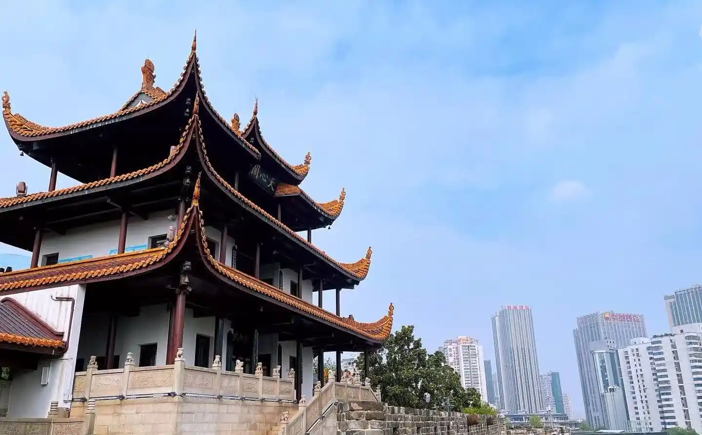 Traditional multi-story Chinese temple with ornate orange-tiled roofs in the foreground and modern high-rise buildings in the background under a blue sky.Tianxin Pavilion,Changsha,Hunan ,Chinatravel