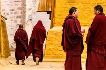 Buddhist monks in maroon robes walk along a sunlit alley with yellow walls.Sera Monastery,Lhasa,Tibet,Chinatravel