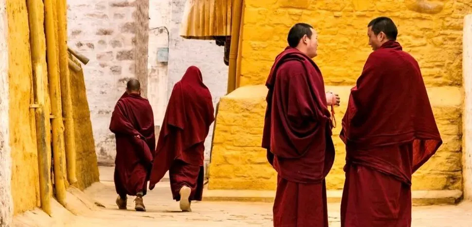 Buddhist monks in maroon robes walk along a sunlit alley with yellow walls.Sera Monastery,Lhasa,Tibet,Chinatravel