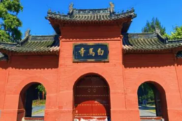 White Horse Temple,Luoyang,Chinatour Red temple gate with curved gray-tiled roof, orange-red walls, and a central arched door beneath a black plaque with gold Chinese characters.