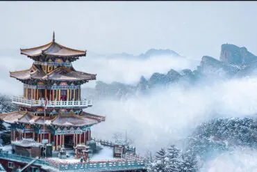 Baiyun Mountain Scenic Area,Luoyang,Chinatour Snow-covered Chinese pagoda perched on a hillside with misty mountains in the background.