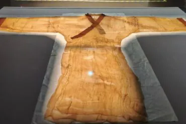 Ancient tan tunic on display in a museum case, with a brown cross-style sash across the chest and long flowing sleeves.Hunan Provincial Museum,Changsha,Hunan ,Chinatravel