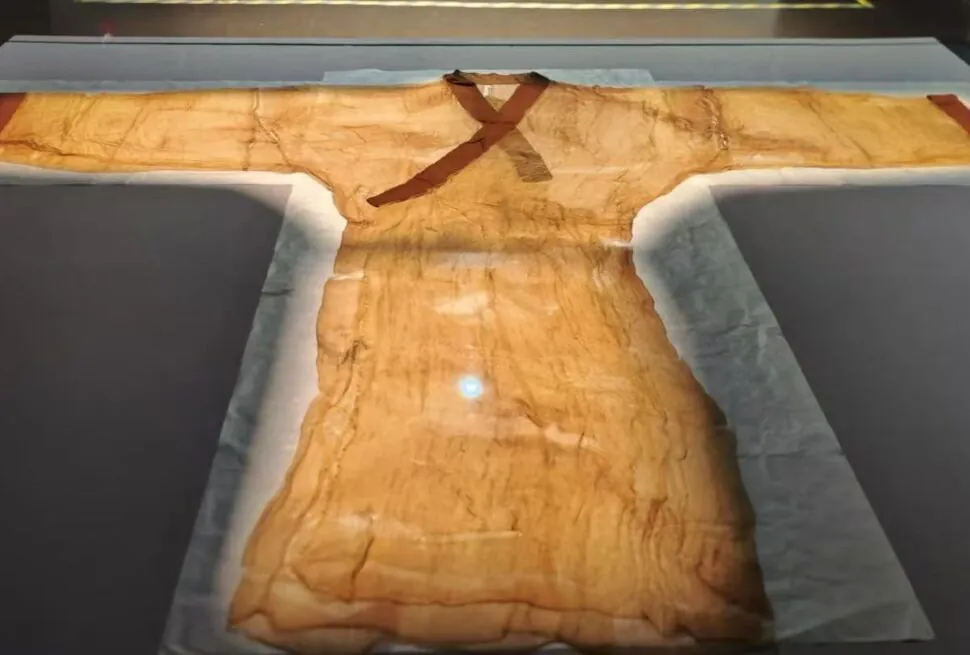Ancient tan tunic on display in a museum case, with a brown cross-style sash across the chest and long flowing sleeves.Hunan Provincial Museum,Changsha,Hunan ,Chinatravel