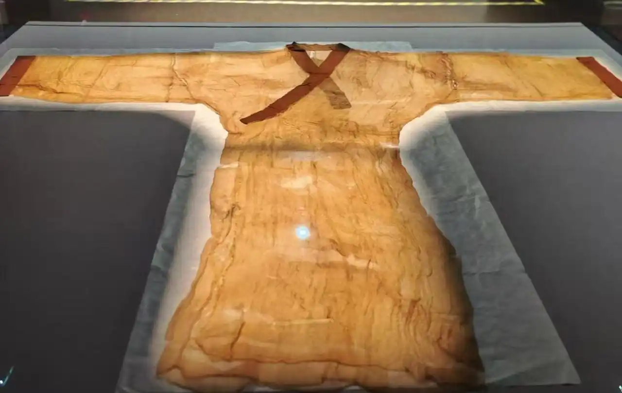 Ancient tan tunic on display in a museum case, with a brown cross-style sash across the chest and long flowing sleeves.Hunan Provincial Museum,Changsha,Hunan ,Chinatravel