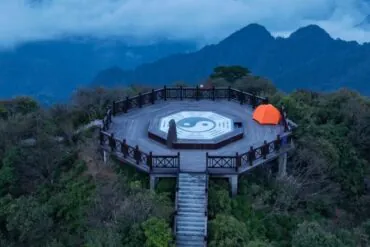 Circular wooden lookout platform on a hill with a large Yin-Yang symbol at center, orange tent to the right, surrounded by mountains and misty blue sky.Sanqing Mountain Scenic Area,Shangrao,Jiangxi,Chinatravel