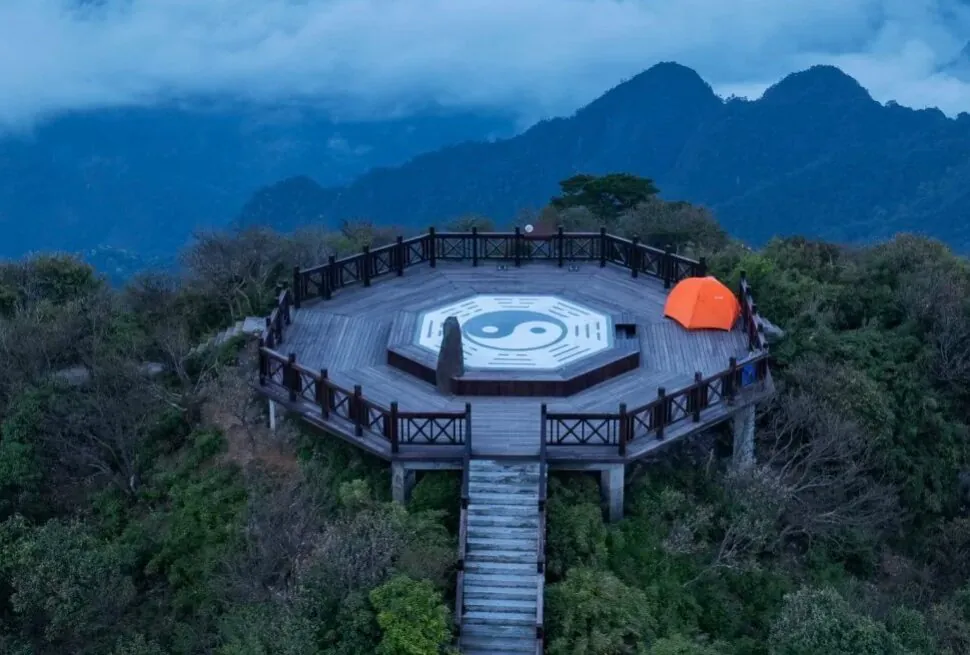 Circular wooden lookout platform on a hill with a large Yin-Yang symbol at center, orange tent to the right, surrounded by mountains and misty blue sky.Sanqing Mountain Scenic Area,Shangrao,Jiangxi,Chinatravel