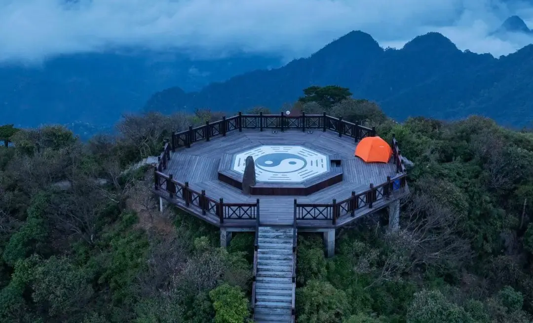 Circular wooden lookout platform on a hill with a large Yin-Yang symbol at center, orange tent to the right, surrounded by mountains and misty blue sky.Sanqing Mountain Scenic Area,Shangrao,Jiangxi,Chinatravel