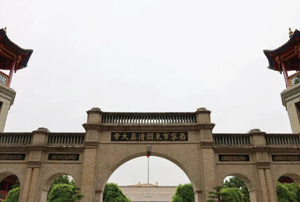 Stone arch gateway in a temple complex, with a central arch flanked by two towers featuring red, pagoda-style roofs and gold Chinese characters on plaques beneath.Dongguan Mosque,Xining,Qinghai