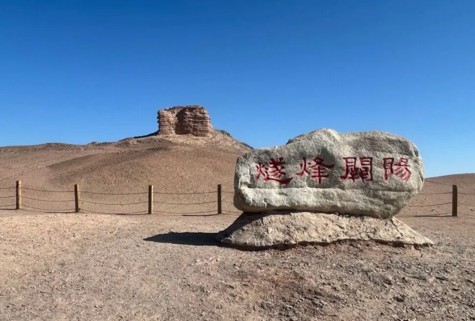 Desert landscape with a large rock inscribed in red Chinese characters and a low wooden post fence in the foreground.Yangguan Ancient Pass,Dunhuang,Gansu