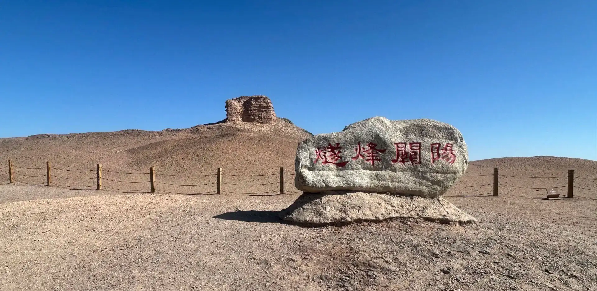 Desert landscape with a large rock inscribed in red Chinese characters and a low wooden post fence in the foreground.Yangguan Ancient Pass,Dunhuang,Gansu