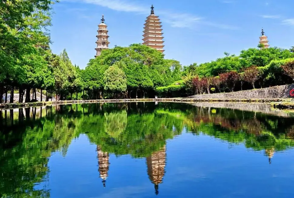 Three-tiered pagodas rise above a green park, reflected in a calm lake.Dali Three Pagodas,Dali,Yunnan,Chinatravel