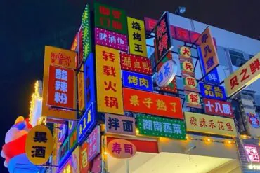 Bright neon restaurant signs with Chinese characters stacked on a corner building at night, creating a colorful storefront wall.Zhengyang Pedestrian Street,Guilin,Guangxi ,Chinatravel