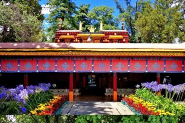 Colorful temple entrance with red canopy, decorative patterns, and blooming purple, yellow, and red flowers lining a stone path,Norbulingka Park,Lhasa,Tibet,Chinatravel