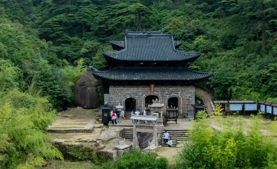 Traditional stone temple with dark tiled, multi-tiered roof nestled in a dense green forest; visitors at the entrance.Sanqing Mountain Scenic Area,Shangrao,Jiangxi,Chinatravel