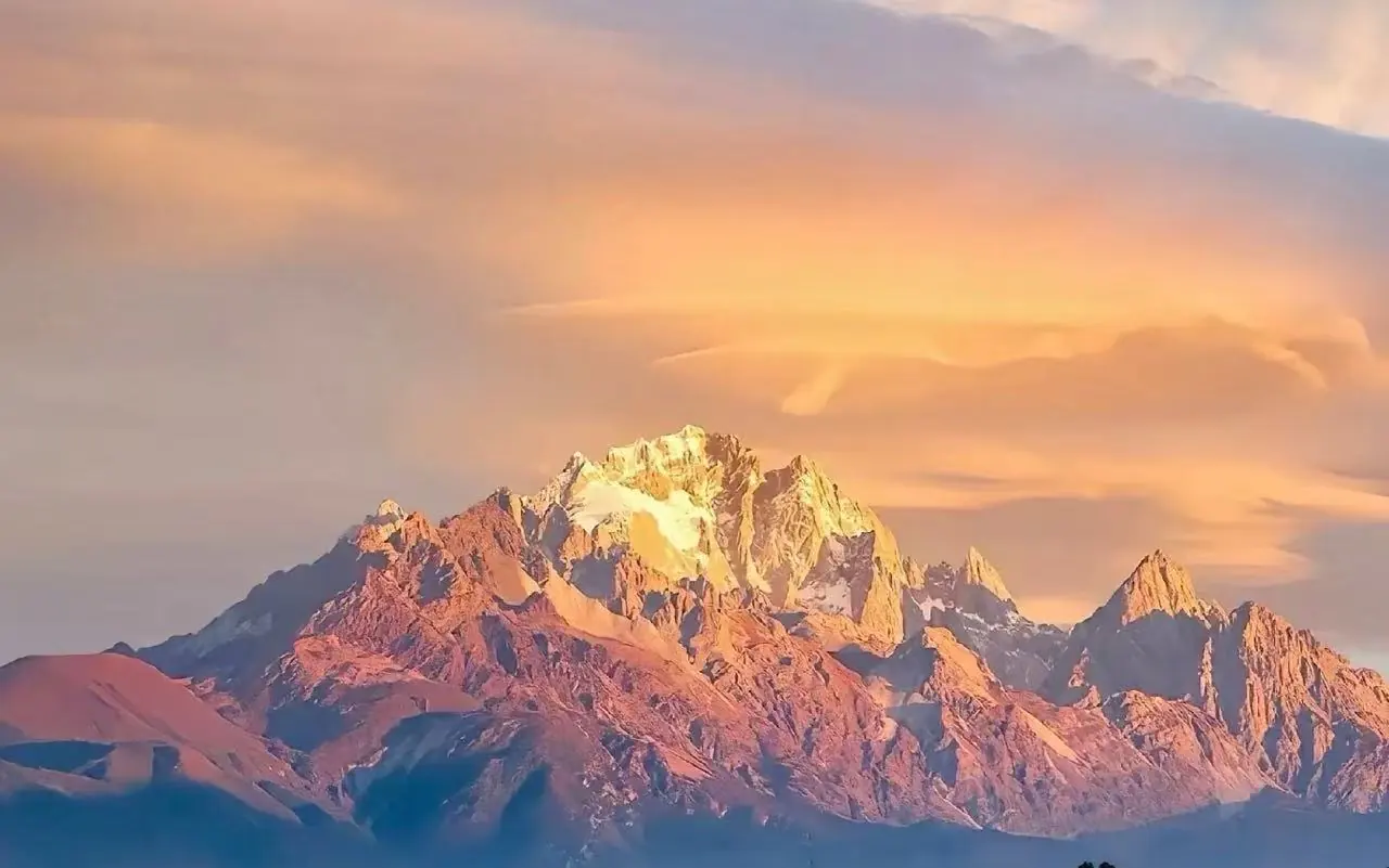 Snow-capped mountain range bathed in warm sunset light against a pastel sky,Jade Dragon Snow Mountain,Lijiang,Yunnan,Chinatravel