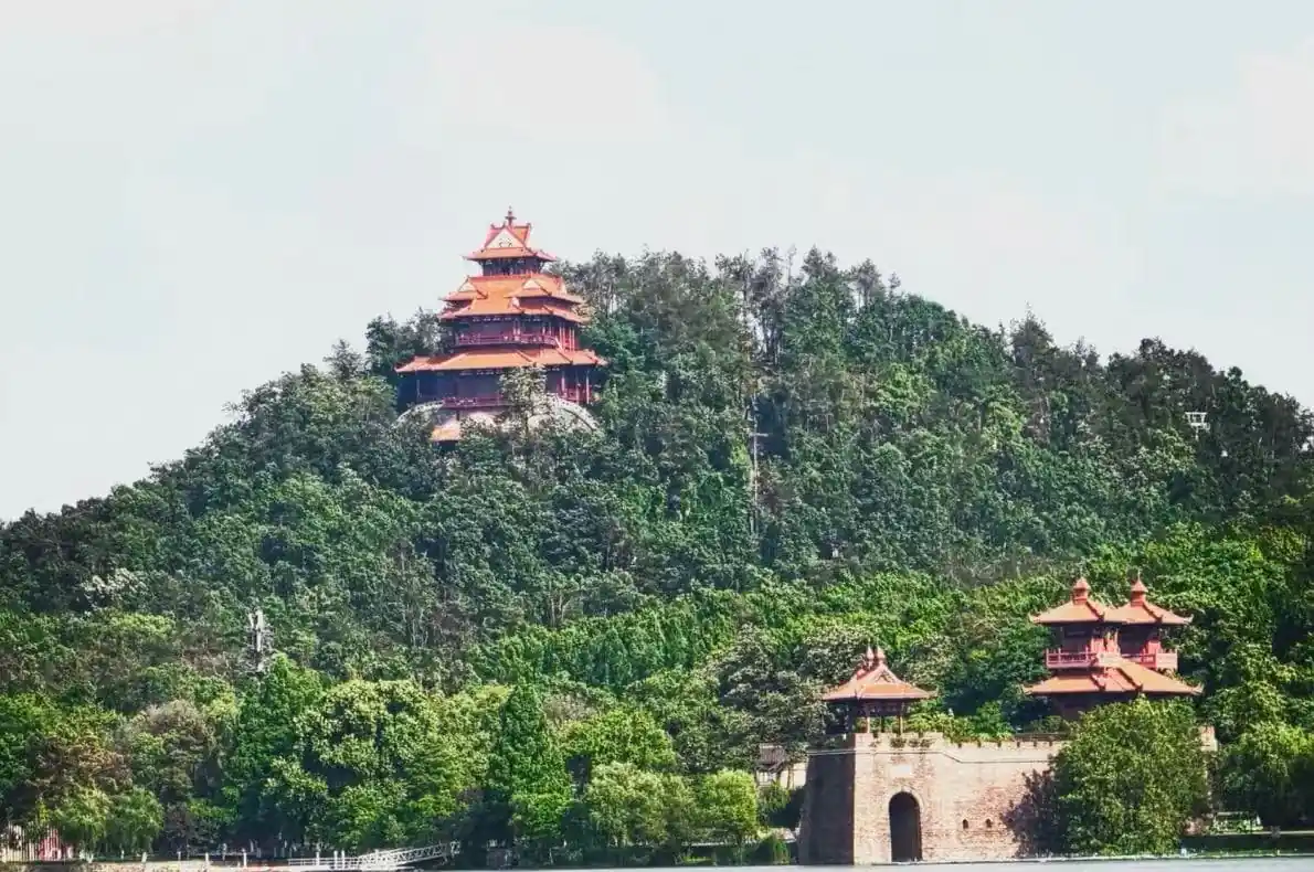 Red multi-tiered pagodas atop a forested hill beside the lake, with a stone gate at the shore in the foreground.Moshan Hill & Botanical Gardens,Wuhan,Hubei ,Chinatravel