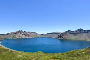 Baishan West Slope Scenic Area,Baishan,Jilin,Chinatravel Bright blue alpine lake nestled in a circular crater, with green slopes and rugged mountain peaks under a clear sky.
