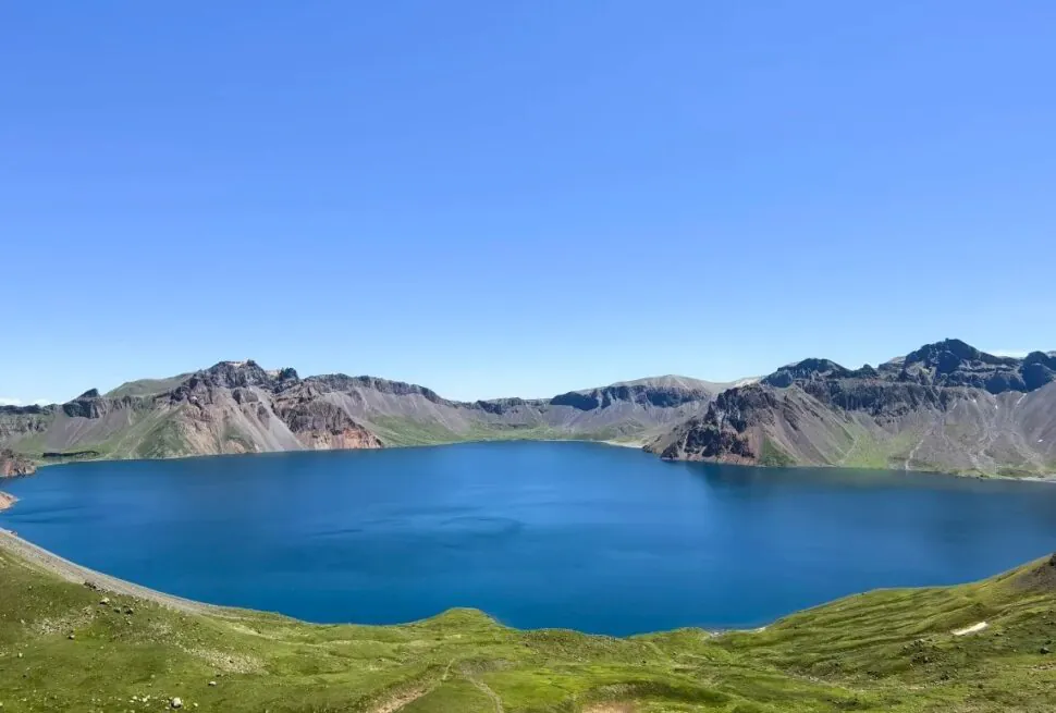 Baishan West Slope Scenic Area,Baishan,Jilin,Chinatravel Bright blue alpine lake nestled in a circular crater, with green slopes and rugged mountain peaks under a clear sky.