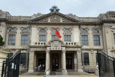 Lushun (Port Arthur) Historic District,Dalian,Liaoning,Chinatravel Front view of a grand historic building with ornate stonework, large arched windows, and a Chinese flag at the entrance.