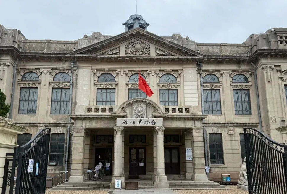 Lushun (Port Arthur) Historic District,Dalian,Liaoning,Chinatravel Front view of a grand historic building with ornate stonework, large arched windows, and a Chinese flag at the entrance.
